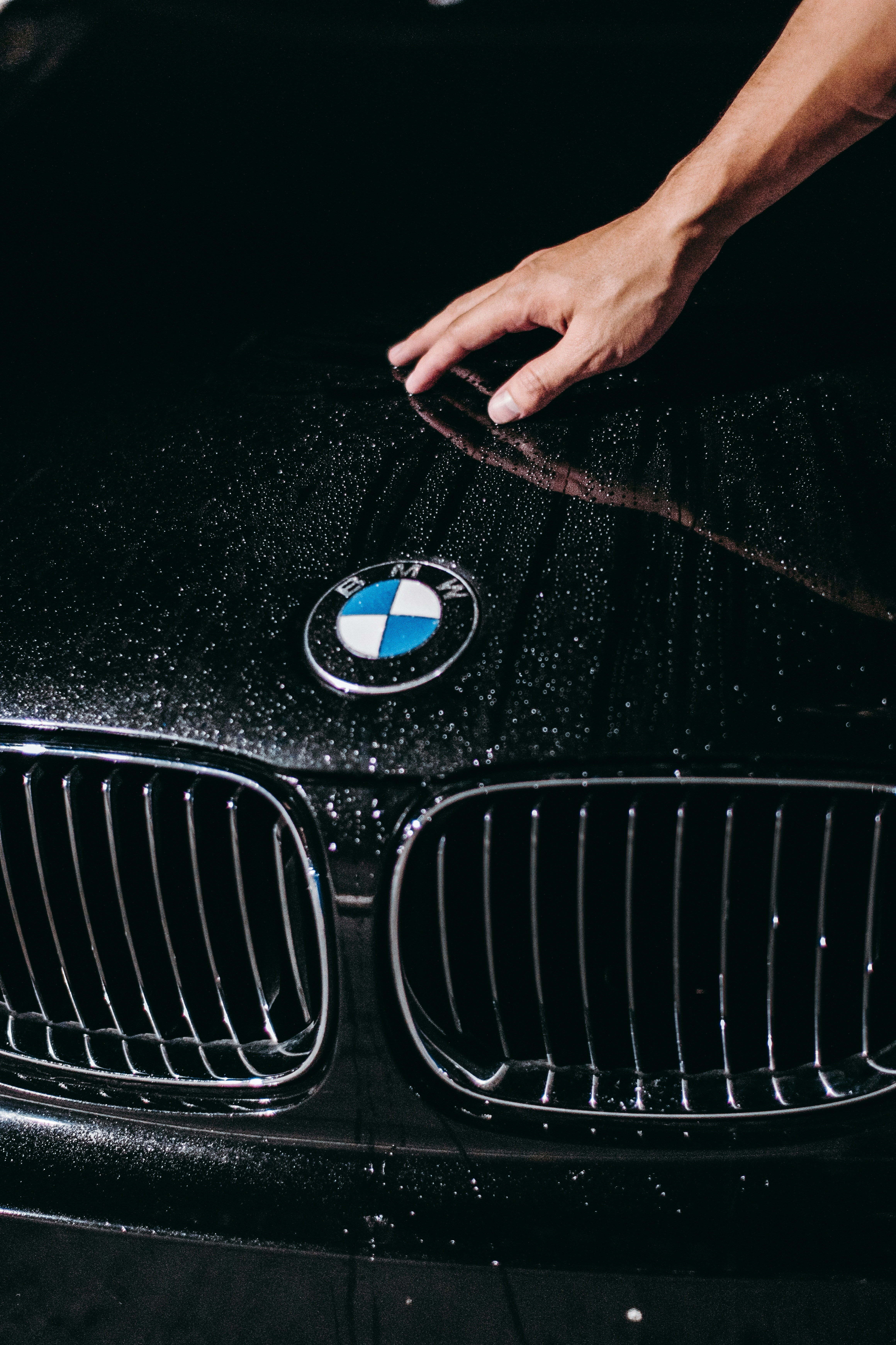 Hand auf einer dunklen Motorhaube mit feinen Wasserperlen